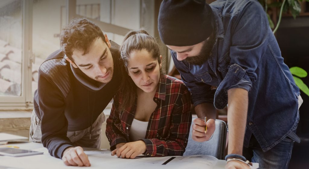 Three people leaning over one set of plans, working it out together